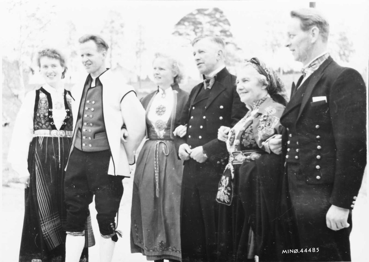 Schwarz-weißes Foto einer lachenden Gruppe von Menschen im Freien mit Bäumen im Hintergrund, beschriftet mit "Bayerische Familie in den 1930er Jahren".