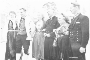 Schwarz-weißes Foto einer lachenden Gruppe von Menschen im Freien mit Bäumen im Hintergrund, beschriftet mit "Bayerische Familie in den 1930er Jahren".