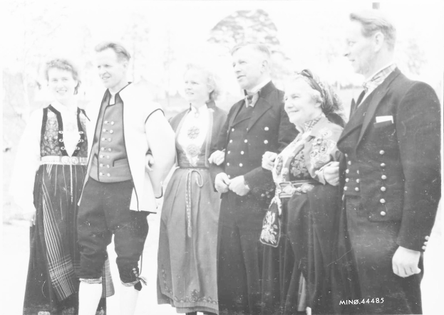 Schwarz-weißes Foto einer lachenden Gruppe von Menschen im Freien mit Bäumen im Hintergrund, beschriftet mit "Bayerische Familie in den 1930er Jahren".