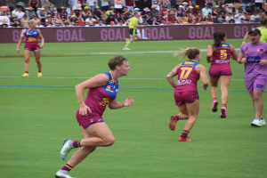 Eine Gruppe von Frauen, die Australian Football League auf einem Rasenfeld spielt, mit Zuschauern im Hintergrund.