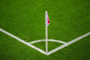 Ein Fußballfeld mit grünem Rasen, weißen Begrenzungslinien und einem weißen Pfosten mit einer roten und weißen Flagge in der Mitte des Elfmeterpunkts.