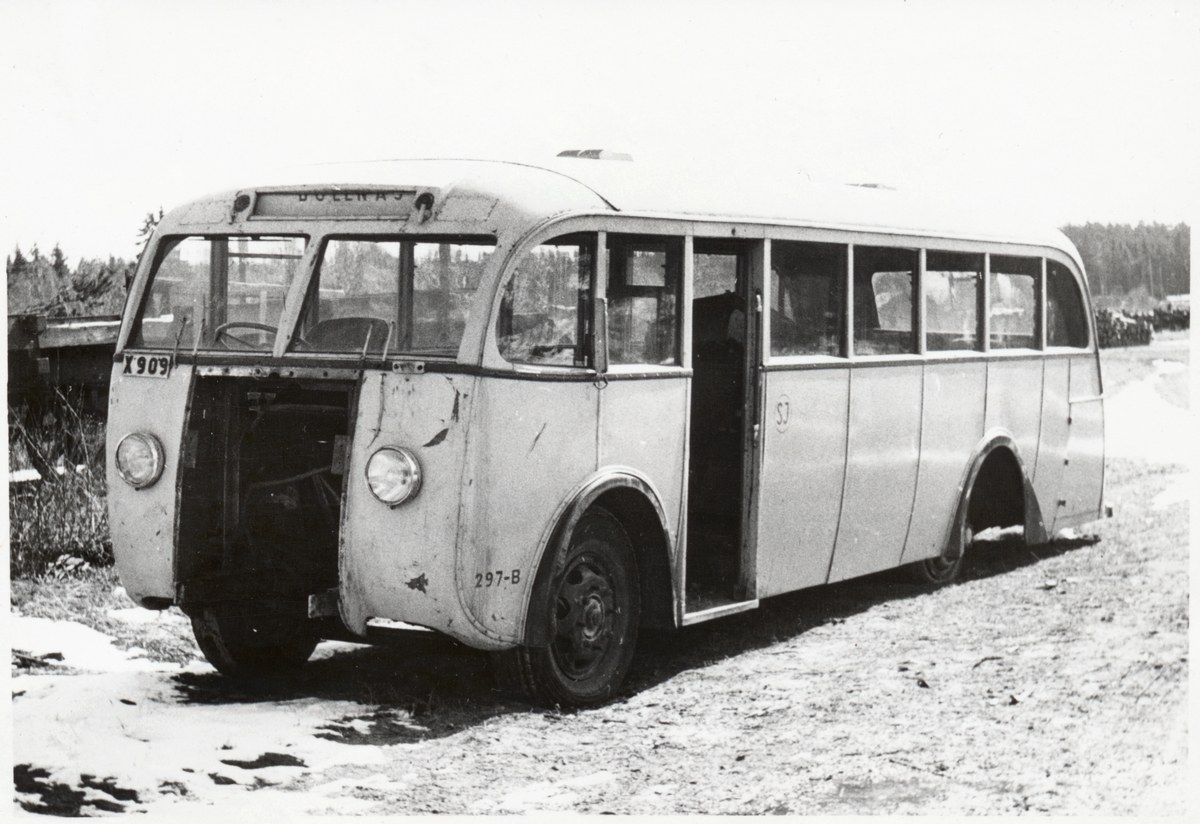 Alter Bus am Straßenrand mit sichtbarem Vorderrad, umgeben von Bäumen unter einem klaren Himmel.