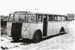 Alter Bus am Straßenrand mit sichtbarem Vorderrad, umgeben von Bäumen unter einem klaren Himmel.