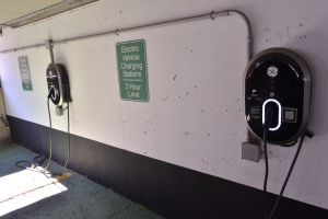 Eine Ladestation für Elektrofahrzeuge in einer Tiefgarage mit zwei Ladesäulen an der Wand und Tafeln mit Text darauf, der Boden ist unten im Bild zu sehen.