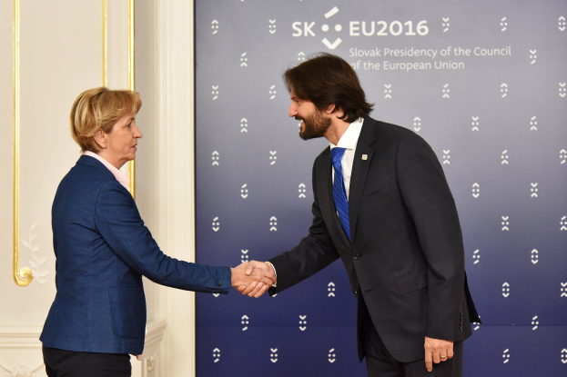 Bundeskanzlerin Angela Merkel und Bundeskanzler Joachim Gauck schütteln sich die Hände vor einem "EU-Gipfel"-Plakat, beide lächeln.