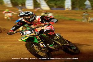 Mehrere Motorradfahrer mit Helmen rasen auf einer Strecke, mit Text am unteren Bildrand.