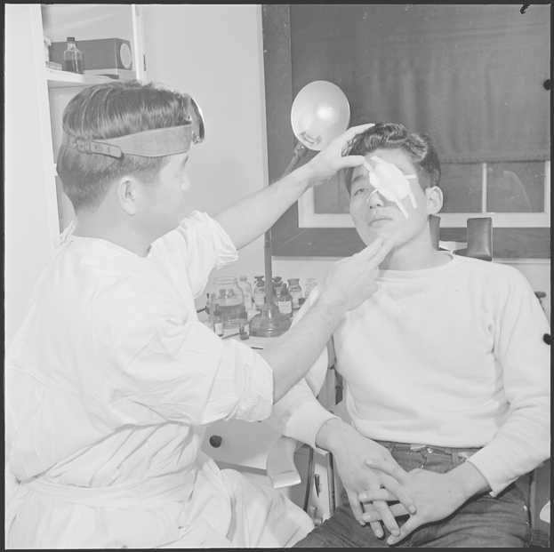 Ein Schwarz-Weiß-Foto eines Mannes, der von einem Arzt untersucht wird, mit medizinischer Ausrüstung und einem Fenster im Hintergrund.