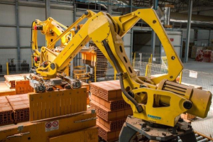 Großes industrielles Lagerhaus mit gestapelten Kisten, Überdachkränen, Zaun, Pfählen und einer fernen Wand in einer Fertigungsumgebung.