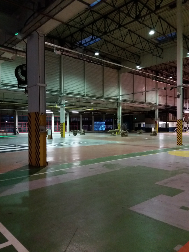 Großes Lagerinnere mit diverser Maschinen, Metallstangen und Beleuchtungsausrüstung, mit Text auf der rechten Bodenfläche.