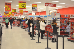 Ein volles Walmart-Geschäft mit Einkaufstaschen tragenden Kunden und Einkaufswagen, umgeben von Warenpräsentationen, Schildern und Deckenleuchten.
