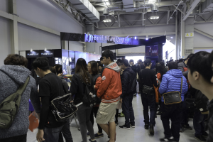 Eine Gruppe von Menschen vor einer Menge auf einer Gaming-Messe, mit Brettern, Lichtern und Rohren im Hintergrund.