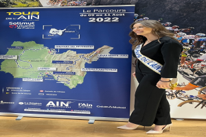 Eine Frau steht vor einer Fahne mit einer Karte von Frankreich, auf der ein Band mit der Aufschrift "Tour de France 2020" trägt.