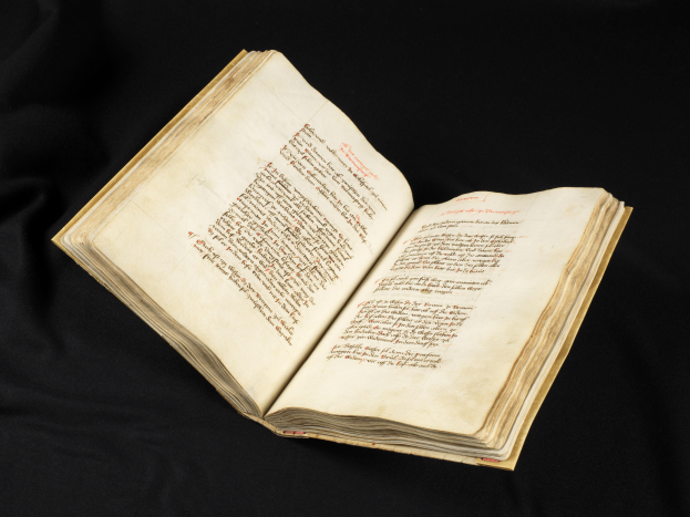 Ein aufgeschlagenes Buch mit rotem Text auf den Seiten, vor schwarzem Hintergrund.