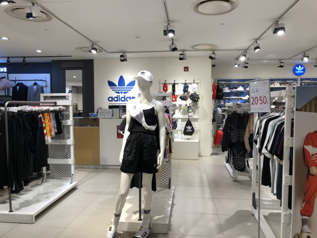 Innenansicht eines Adidas-Geschäfts in Singapur mit Schaufensterpuppen, Kleiderständern, einer Texttafel auf der rechten Seite und Deckenbeleuchtung.