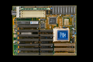 Eine Leiterplatte mit einem zentralen CPU-Chip, der Text anzeigt, umgeben von Widerständen, Kondensatoren und Transistoren.
