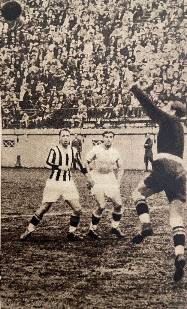 Schwarzes und weißes Foto von Männern, die Fußball spielen, mit Zuschauern auf den Tribünen und einer Wand im Hintergrund, beschriftet mit 'Newcastle United v West Bromwich Albion'.