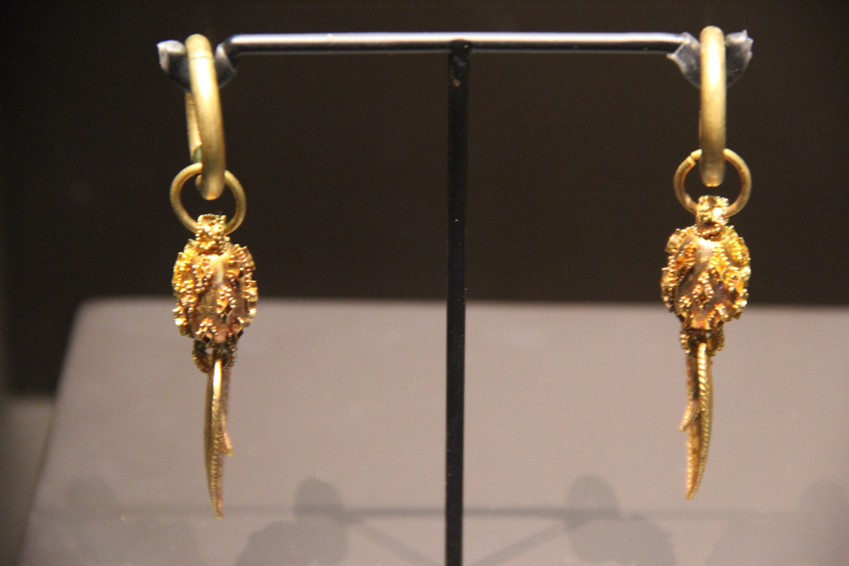 Goldene Ohrringe in einer Glasvitrine auf einem Ständer präsentiert.