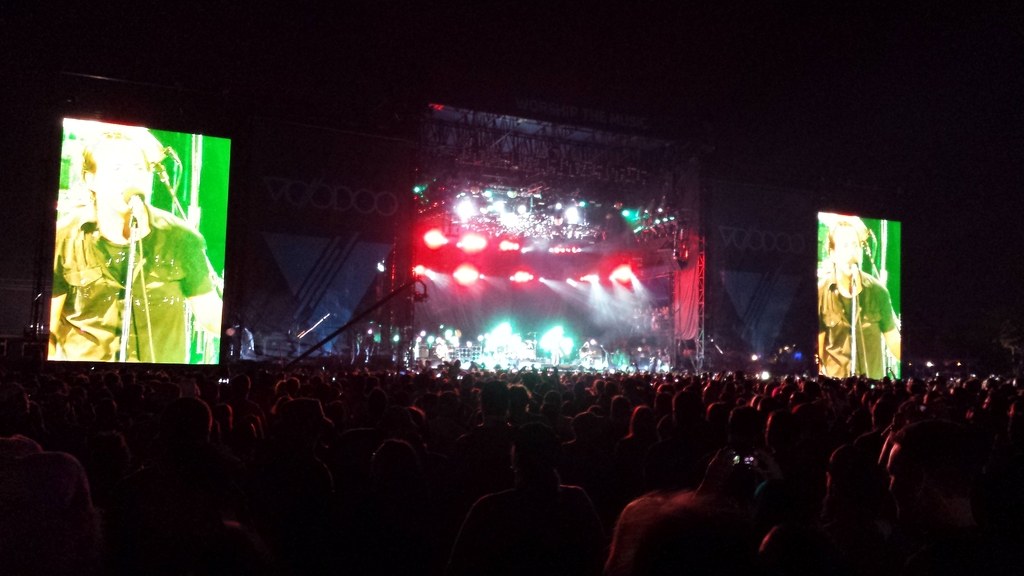 Bühne mit Publikum darunter, flankiert von großen Bildschirmen links und rechts.