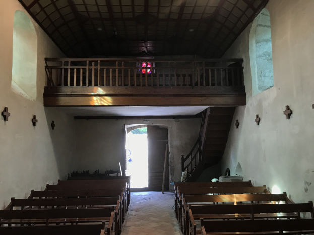 Inneneinrichtung einer Kirche mit hölzernen Bänken, gefliestem Boden, Kreuzen an den Wänden, Geländern, Treppen mit Geländern, einer Hintertür und einem Bleiglasfenster.