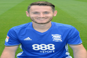 Ein Mann sitzt auf einem Fuballfeld in einem blauen T-Shirt, lächelt und hat einen Trainings-Session-Text unten.