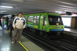 Ein Zug auf einer Schienenstraße mit Menschen auf der linken Seite und einem Dach oben im Bild.
