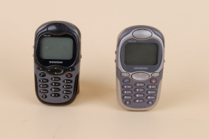 Zwei alte Funktelefon-artige Mobiltelefone mit glänzendem schwarzen Finish auf einer cremefarbenen Oberfläche.