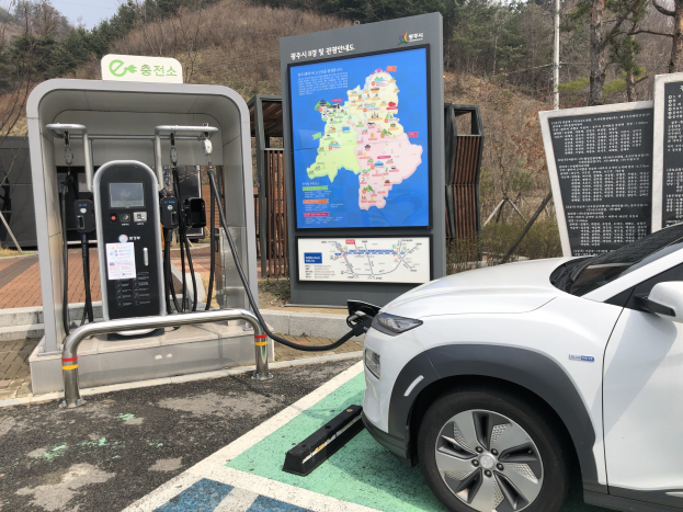 Ein Elektroauto, das an einer Station in Seoul, Südkorea, geladen wird, umgeben von Bäumen mit dem Himmel im Hintergrund.