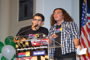 Drinnen ein Podium mit zwei Mikrofonen und Texttafeln in der Mitte, Ballons auf der linken Seite und eine Flagge auf der rechten Seite, mit einer Wand im Hintergrund.