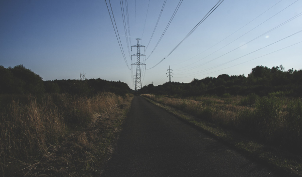 Straße mit Stromleitungen im Freien, flankiert von grünem Gras und Bäumen, die zu Übertragungstürmen führen