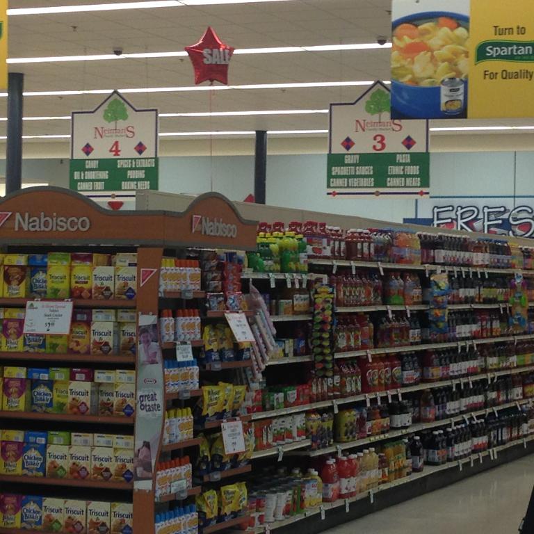 Ein Supermarkt-Innenraum mit Regalen voller Lebensmittel, Deckenleuchten und Schildern.