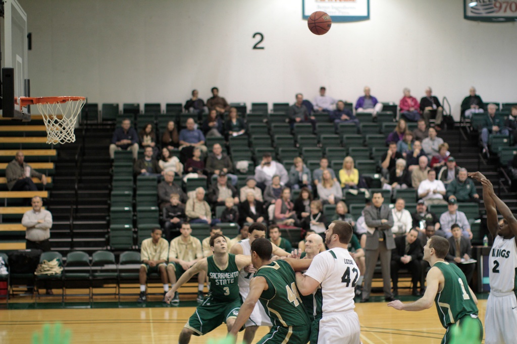 Ein Basketballspiel im Gange mit Spielern auf dem Feld und Zuschauern im Hintergrund.