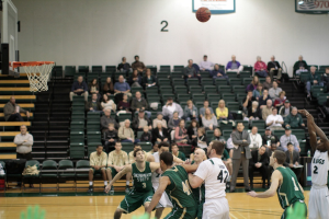 Ein Basketballspiel im Gange mit Spielern auf dem Feld und Zuschauern im Hintergrund.
