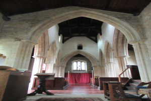 Das Innere einer Kirche mit Gewölben, Säulen, Stühlen, Tischen, einem Teppichboden, einem hölzernen Gegenstand links, Treppen mit Geländern, einer Wand mit einem Fenster und einem Vorhang im Hintergrund und einer hölzernen Decke.