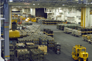 Ein gro├če Lagerhalle-Innensicht mit zahlreichen LKW, Containern, Menschen, Lichtern, St├Ąben und anderen Objekten, mit einem prominenten Rad.