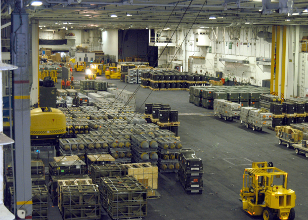 Ein gro├če Lagerhalle-Innensicht mit zahlreichen LKW, Containern, Menschen, Lichtern, St├Ąben und anderen Objekten, mit einem prominenten Rad.