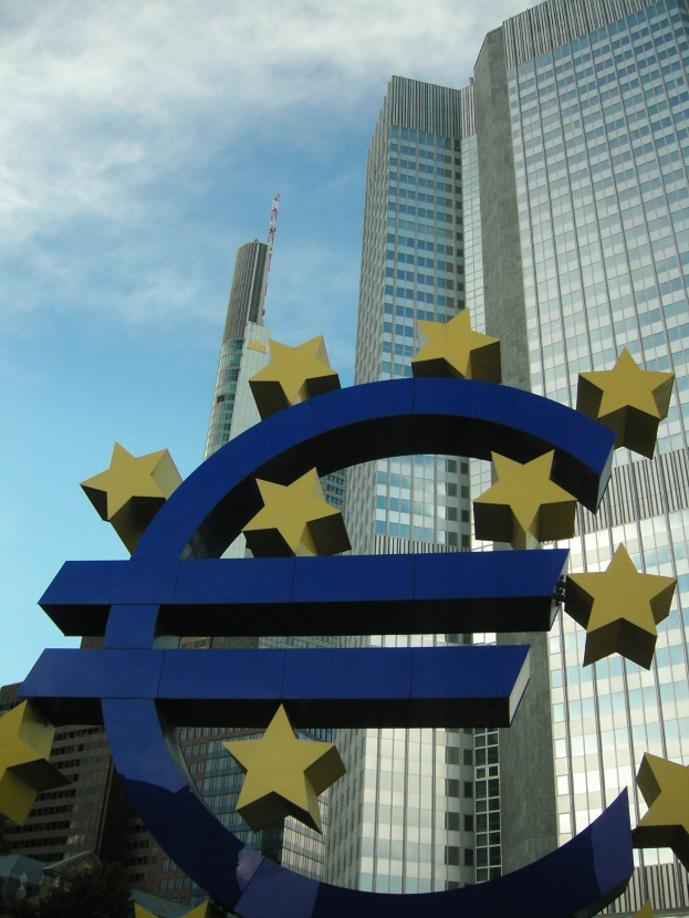 Euro-Zeichen vor dem Hauptsitz der Europäischen Zentralbank in Frankfurt, Deutschland, mit Bäumen und einem bewölkten Himmel im Hintergrund.