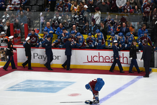 Ein Eishockeyspieler auf dem Eis umgeben von Teamkollegen und Gegnern, mit Zuschauern im Hintergrund während eines Spiels zwischen Colorado Avalanche und San Jose Sharks am 24. März 2015.