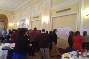 Eine Gruppe von Menschen untersucht Plakate und Diagramme, die an einer Wand in einem Kunstmuseum zu sein scheinen.