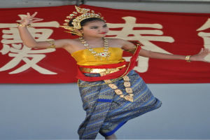 Ein M├Ądchen tanzt in einem kulturellen Kleid und Schmuck, mit einem Banner mit Text dahinter.