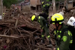 Feuerwehrleute mit Helmen und Taschen durchsuchen die Trümmer eines eingestürzten Gebäudes in Mexiko-Stadt, umgeben von Bäumen, anderen Gebäuden und verstreuten Holzstöcken.