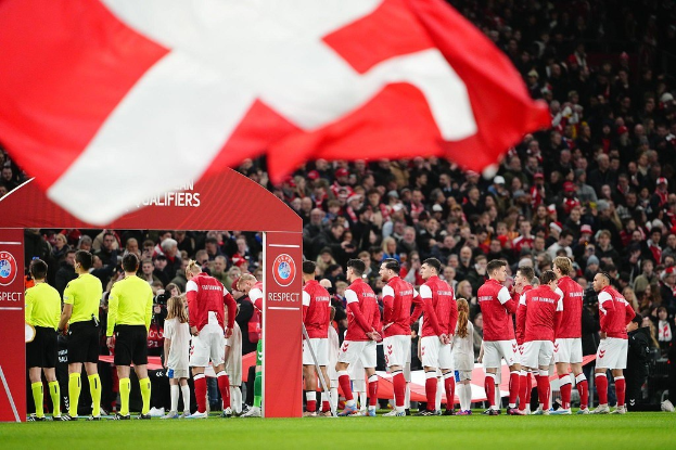 Gruppe von Menschen auf einem Fußballfeld mit einer roten und weißen Flagge im Vordergrund, einem Bogen mit der Aufschrift "Bayern München vs Bayern München Wett-Tipps & Vorschau" im Hintergrund und einer großen Menge im Stadion.