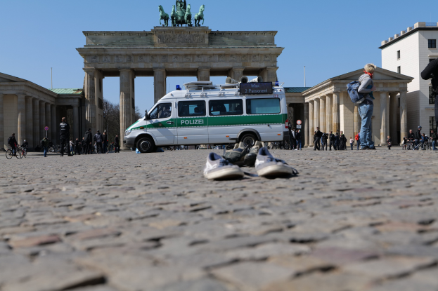 Polizeifahrzeug vor dem Reichstag mit Menschen, Fahrrädern und einem weggeworfenen Schuh in der Nähe, vor historischem Architekturhintergrund und einem klaren Himmel.