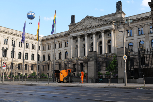Großes modernes Gebäude mit vielen Fenstern, als Bundestag in Berlin, Deutschland identifiziert, umgeben von Straßenmöbeln, Fahrzeugen, Fußgängern und Bäumen unter einem bewölkten Himmel.