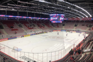 Eishockeyspiel in einer großen Arena zwischen den St. Louis Blues und Detroit Red Wings, mit Zuschauern auf den Sitzen und Stehplätzen in der Nähe des Spielfelds umgeben von einem Zaun und Anzeigetafeln.