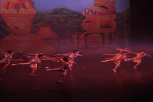 Menschen in Kostümen, die auf einer Bühne mit einem Vorhang im Hintergrund auftreten.