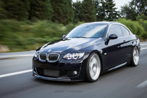 Ein schwarzes BMW-Auto fährt auf einer Straße mit Bäumen im Hintergrund.