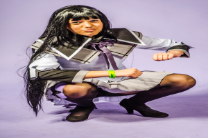 Eine Person in einem Kostüm lächelt, während sie auf einem violetten Hintergrund hockt.