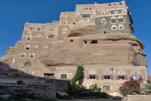 Ein Schloss mit Fenstern und Türen, umgeben von Pflanzen, unter einem blauen Himmel.