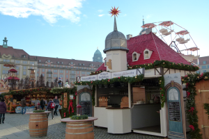 Ein lebendiger Weihnachtsmarkt in Nürnberg, Deutschland, mit Menschen um geschmückte Buden, Gebäude, ein Riesenrad und einen bewölkten Himmel, mit einer Tafel auf der rechten Seite.