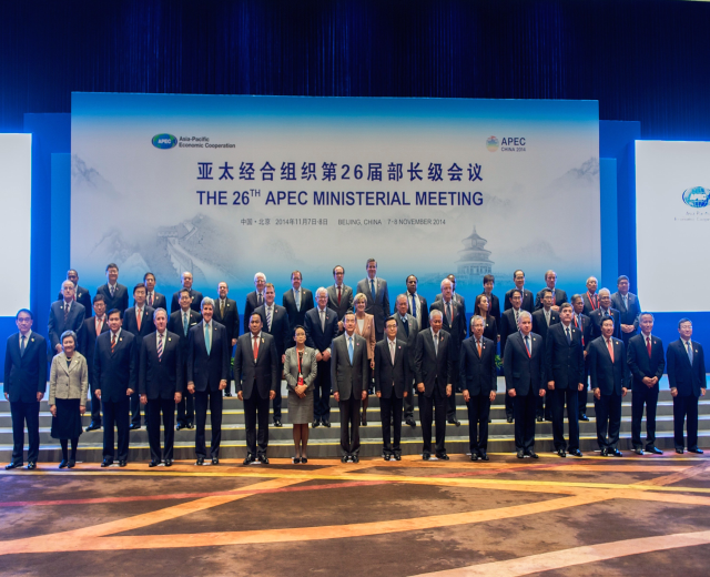Gruppe von Menschen in formeller Kleidung auf einer Bühne mit einem Bildschirm, der "Asia Pacific Economic Cooperation Summit" anzeigt.